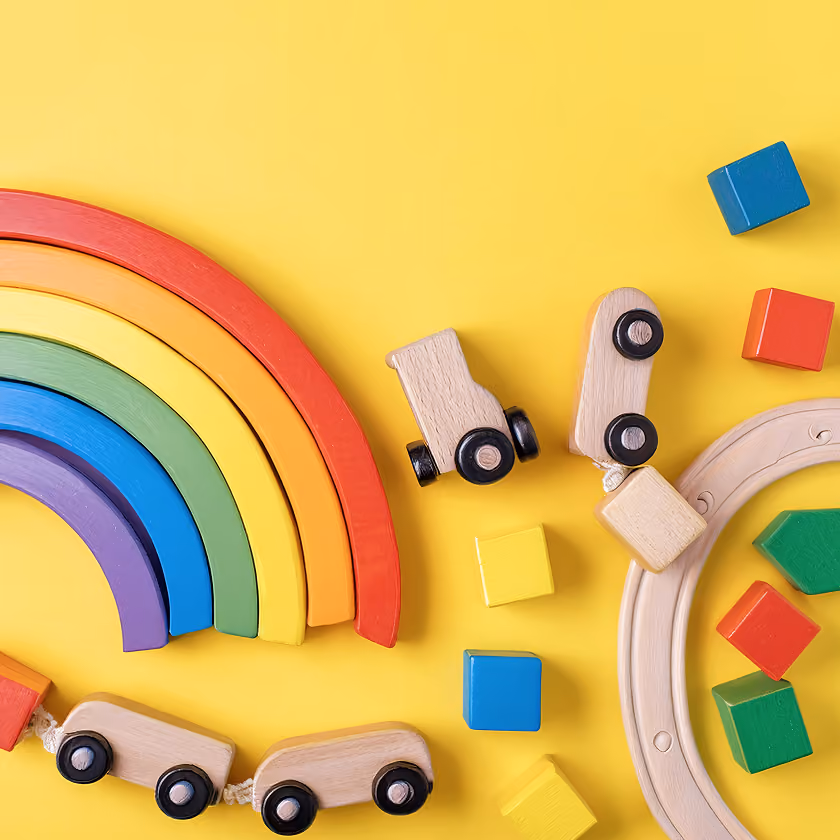 Wooden rainbow toy and wooden train with colorful blocks on a yellow background.